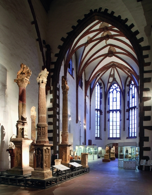 Bild vergrössern: Blick in die Ausstellung im Seitenschiff der Klosterkirche mit Säulen im Vordergrund und Vitrinen im Hintergrund