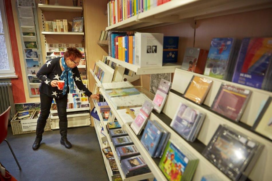 Frau greift in ein Regal mit vielen Büchern und CDs im Shop im Bibelhaus Erlebnis Museum