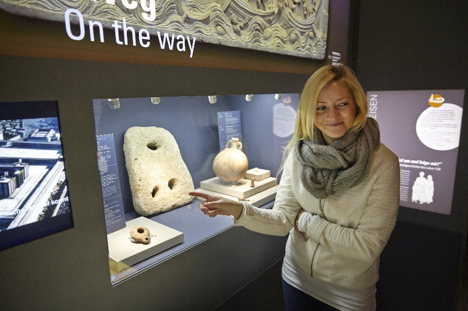 Bild vergrössern: Besucherin zeigt auf Steinobjekt in Vitrine im Bibelhaus Erlebnis Museum