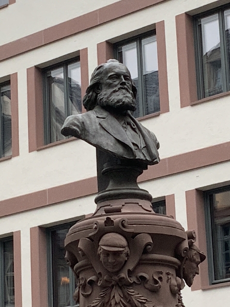 Bild vergrössern: Portraitbüste von Friedrich Stoltze auf dem Stoltze-Platz mit Gebäudefassade im Hintergrund