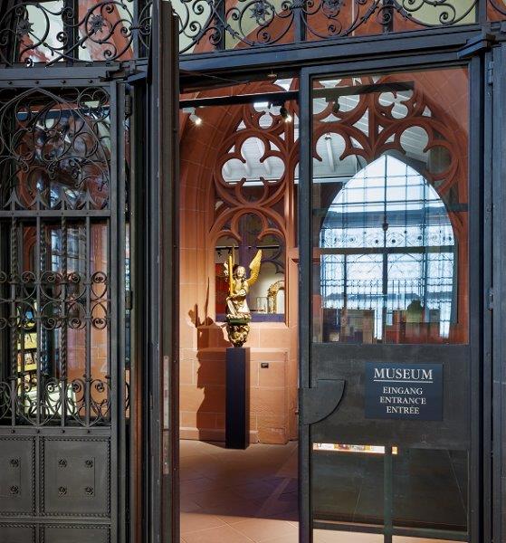 Bild vergrössern: Offene Eingangstür zum Dommuseum mit der Statue eines goldenen Engels auf einem Sockel im Hintergund