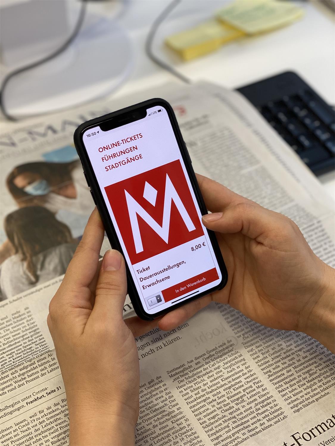 Eine Person hält ein Handy in der Hand, auf dem Display die responsive Ansicht des Museumsshop des Historischen Museums