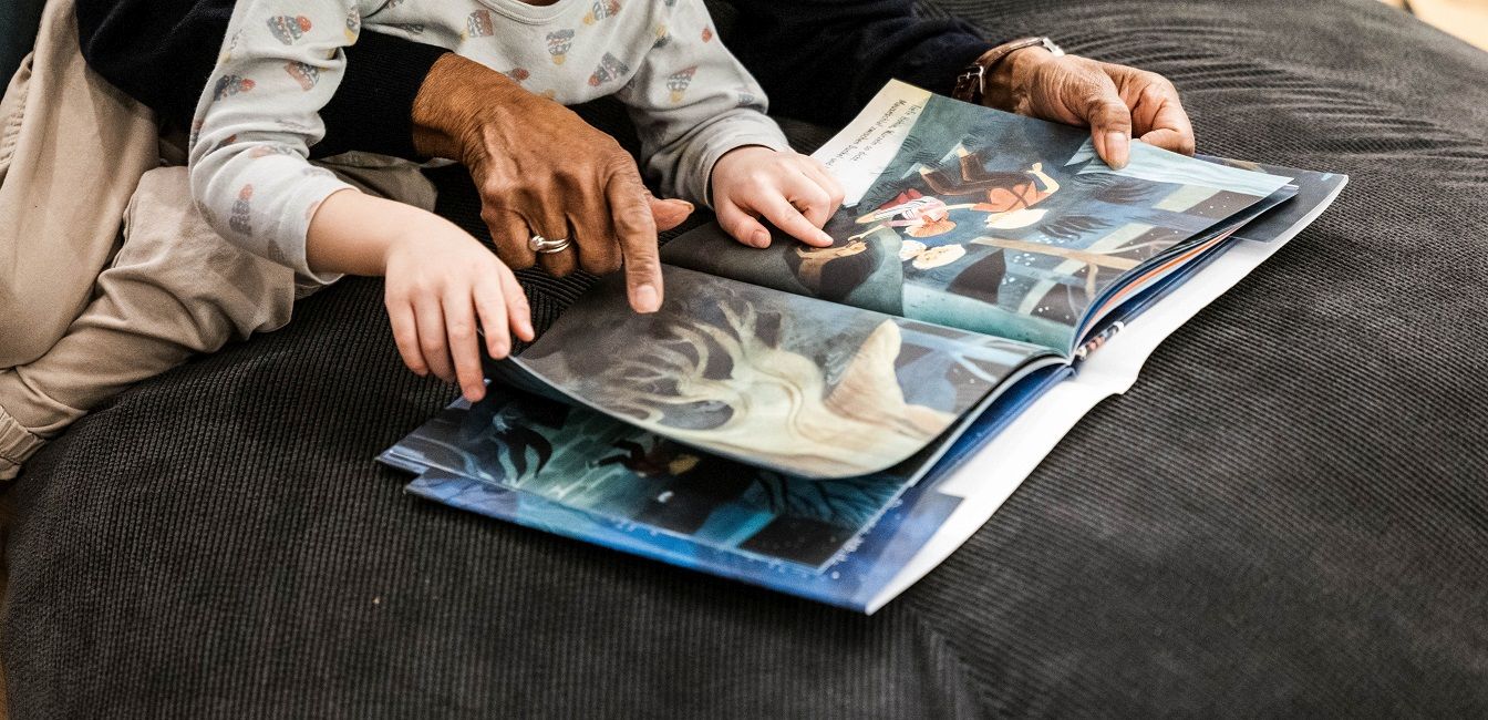 Enlarge image: Hände von einer älteren Person und einem Kind blättern in einem Buch mit großen Fotos