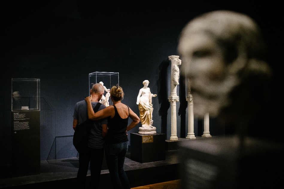 Bild vergrössern: Pärchen (von hinten fotografiert) betrachtet Vitrine zwischen mehreren Skulpturen im Liebieghaus