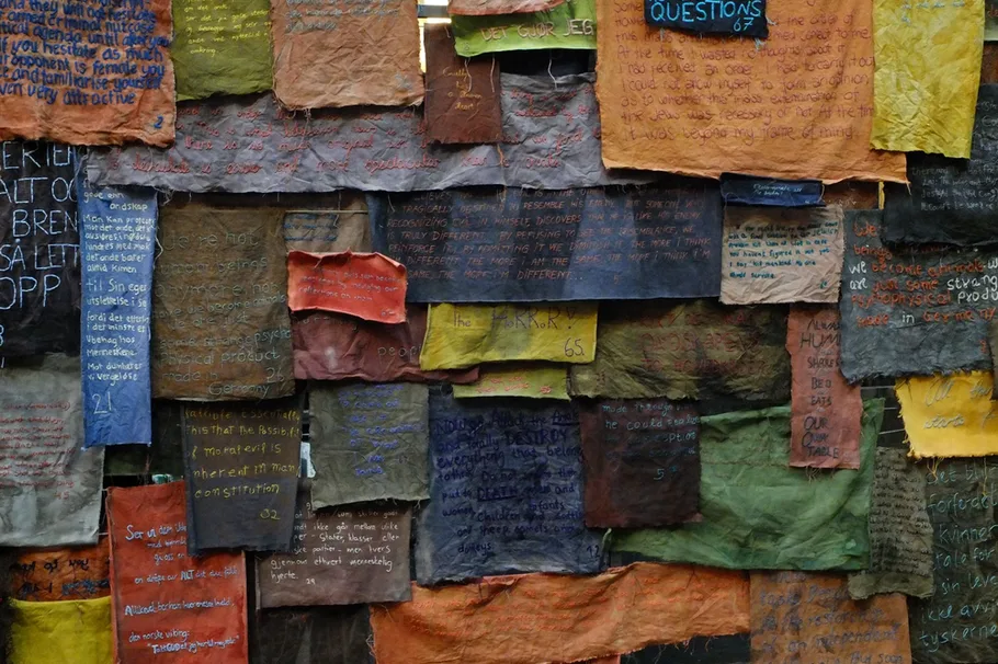 Bild vergrössern: Mit Text bestickte bunte, quadratische Textilst&uuml;cke &uuml;bereinandergeh&auml;ngt