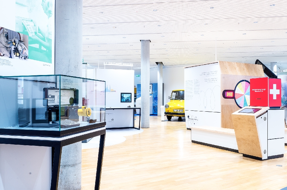 Bild vergrössern: Dauerausstellung des Museums für Kommunikation mit Vitrine im Vordergrund links und gelben Postauto im Hintergrund