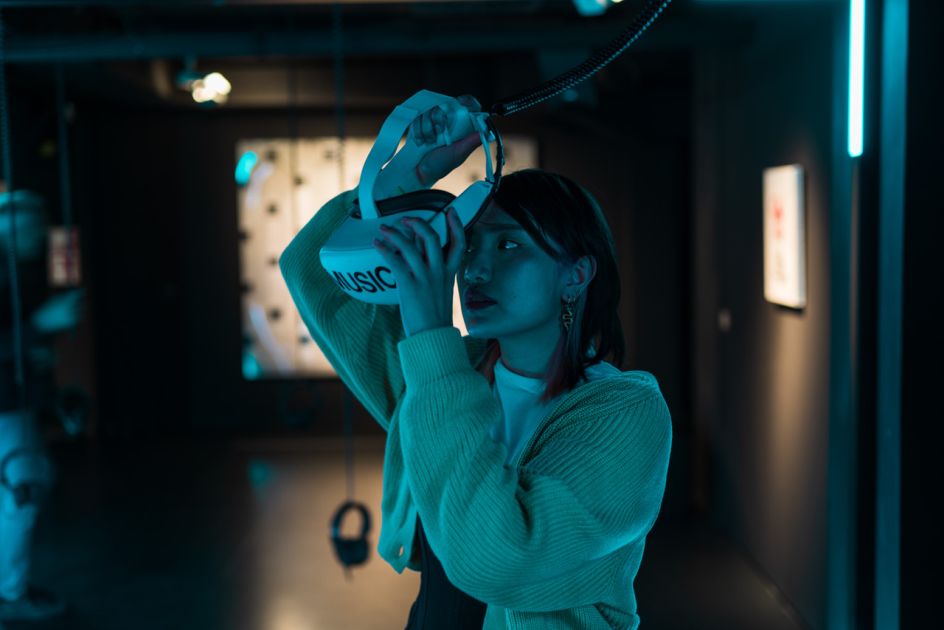 Enlarge image: Besucherin, die VR-Brille mit der Aufschrift &quot;MUSIC&quot; aufsetzt, in der Ausstellung im MOMEM