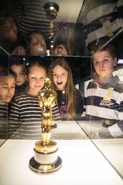 Kinder blicken in Vitrine mit Oscar-Statue im Vordergrund im Filmmuseum