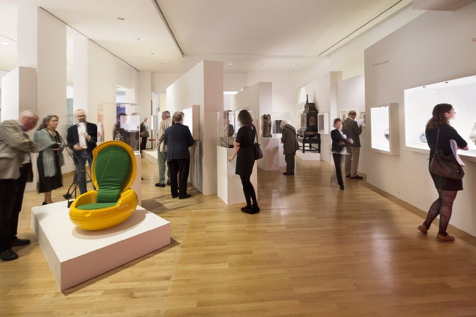 Besucher*innen in der Ausstellung des Museum Angewandte Kunst, modernes Sitzmöbel links im Vordergrund