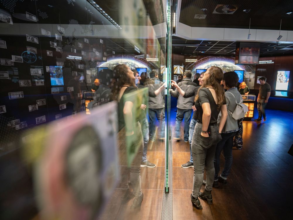 Mehrere Menschen stehen vor einer Vitrine links mit vielen Geldscheinen, im Hintergrund rechts der Ausstellungsraum des Geldmuseums