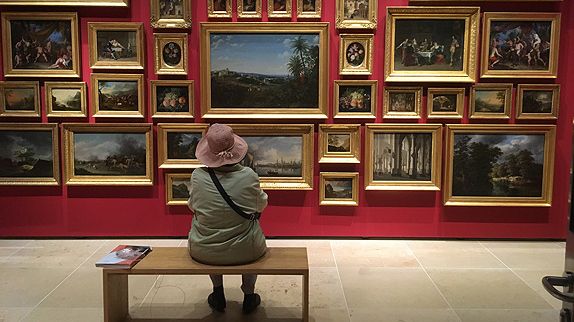 Dame sitzt vor Wand mit vielen Gemälden im Historischen Museum