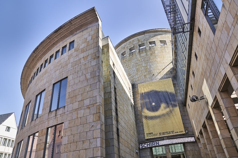 Gebäudeteil der SCHIRN von außen zum Eingang hin fotografiert mit gelbem Ausstellungsplakat mit Auge in der Mitte