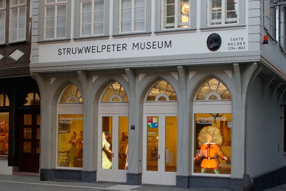 Eingang zum Struwwelpeter Museum mit erleuchteten Fensterbögen und einer Struwwelpeter-Figur im rechten Fenster