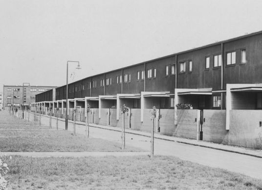 Schwarz-Weiß Fotografie einer Straße mit gleich aussehenden kleinen Reihenhäusern und Gärten mit Rasen