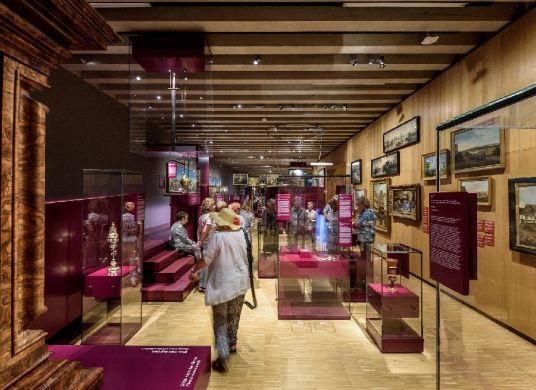 Ausstellung mit Vitrinen und Gemälden sowie Besucher:innen