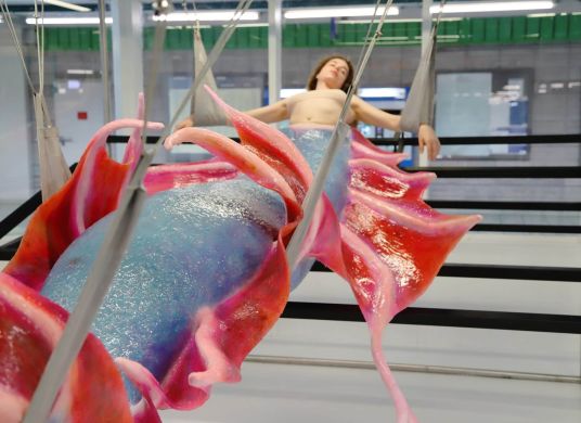 Frau hängt in einem Raum mit rot-blauem Fisch-Kostüm am Unterkörper