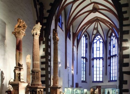 Blick in die Ausstellung im Seitenschiff der Klosterkirche mit Säulen im Vordergrund und Vitrinen im Hintergrund