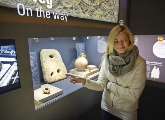 Besucherin zeigt auf Steinobjekt in Vitrine im Bibelhaus Erlebnis Museum