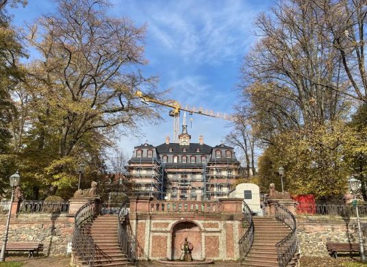 Altes kleines Palastgeb&auml;ude mit Treppenaufg&auml;ngen zu beiden Seiten im Vordergrund und Bauger&uuml;st um das Geb&auml;ude und B&auml;umen