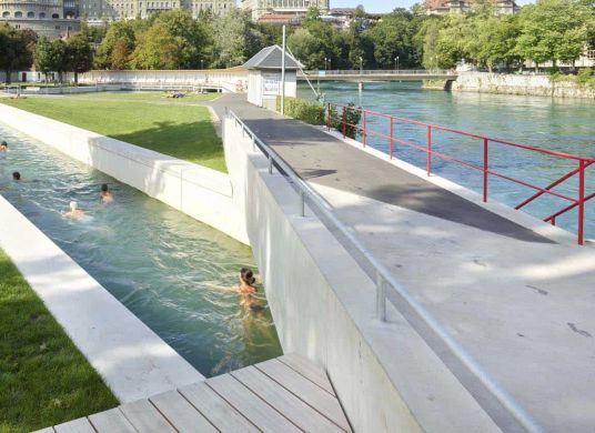 Mehrere Menschen schwimmen in einem Kanal neben einem Fluss in einer Stadt