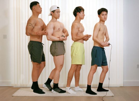 Vier asiatische junge M&auml;nner in Boxershorts stehen hintereinander in Pose, um ihre Muskeln zu zeigen
