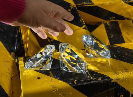 Hand, die nach gro&szlig;en Diamanten greift, die auf einem gelb-schwarzem Untergrund liegen