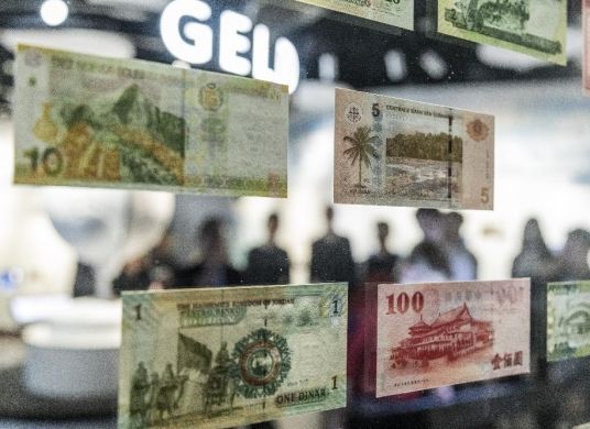 Verschiedene Geldnoten aus verschiedenen Ländern auf einer Glaswand im Ausstellungsraum des Geldmuseums, im Hintergrund eine Personengruppe
