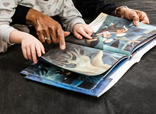 Hände von einer älteren Person und einem Kind blättern in einem Buch mit großen Fotos
