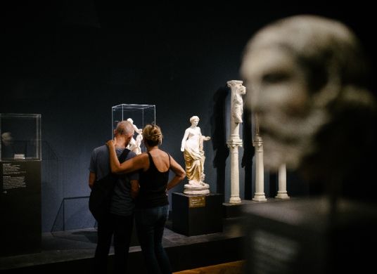 Pärchen (von hinten fotografiert) betrachtet Vitrine zwischen mehreren Skulpturen im Liebieghaus
