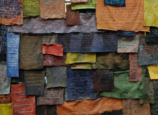 Mit Text bestickte bunte, quadratische Textilst&uuml;cke &uuml;bereinandergeh&auml;ngt