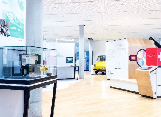 Dauerausstellung des Museums für Kommunikation mit Vitrine im Vordergrund links und gelben Postauto im Hintergrund