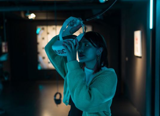 Besucherin, die VR-Brille mit der Aufschrift "MUSIC" aufsetzt, in der Ausstellung im MOMEM