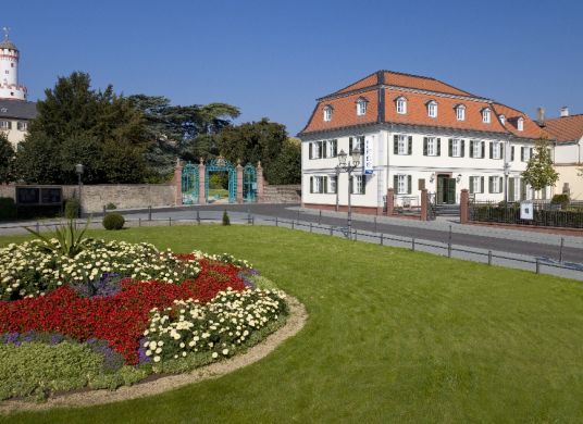 Museum Sinclair-Haus vom gegenüberliegenden Platz mit Wiesen und Blumenbepflanzung im Vordergund links und Turm des Schlosses im Hintergrund links