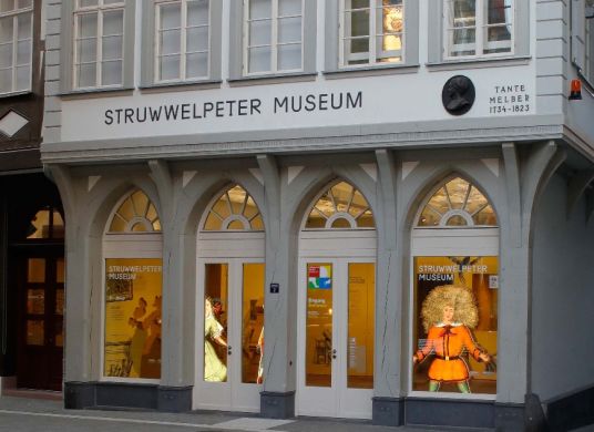 Eingang zum Struwwelpeter Museum mit erleuchteten Fensterbögen und einer Struwwelpeter-Figur im rechten Fenster