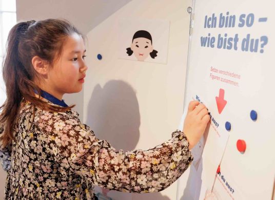 Ein Mädchen schreibt an eine Wand auf der steht 'Ich bin so. Wie bist Du?'