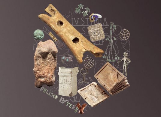 Verschiedene archäologische Objekte wie eine Knochenflöte, Steinfiguren, Schmuck und ein altertümliches Buch zu einem Kreis angeordnet