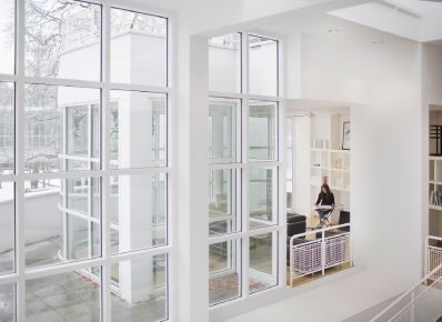 Modernes Gebäude mit viel Fensterfläche von innen und Lesebereich mit lesender Frau im Hintergrund