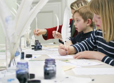 Kinder sitzen rechts an einem Tisch und schreiben mit der Feder im Goethe-Museum