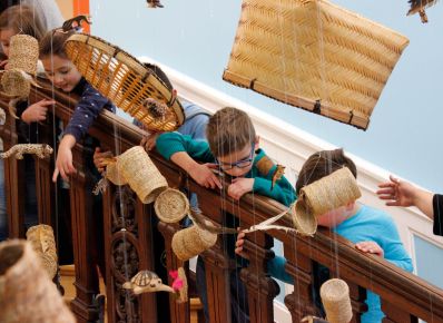 Kinder schauen auf hängende Korbgeflechte im Treppenhaus des Weltkulturen Museums