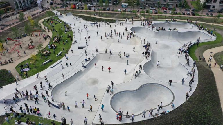Gro&szlig;er Skatepark aus Beton mit verschiedenen Rampen von oben fotografiert mit vielen Menschen, drumherum Wiesen