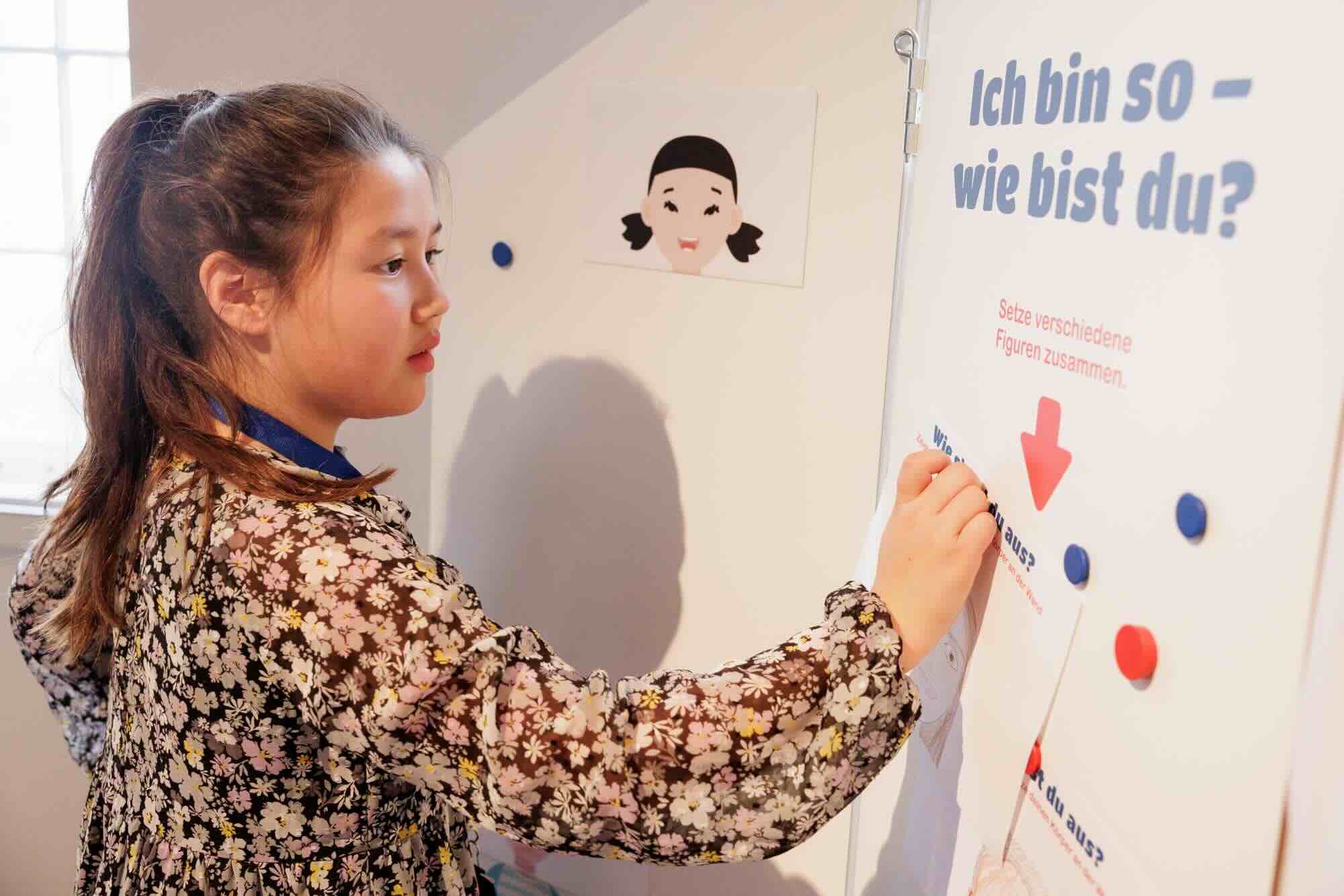 Bild vergrössern: Ein Mädchen schreibt an eine Wand auf der steht 'Ich bin so. Wie bist Du?'