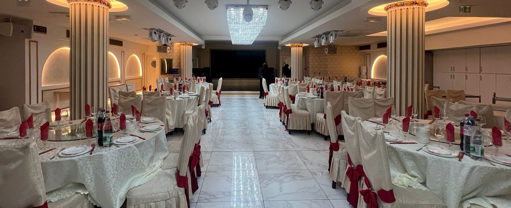 Enlarge image: Dieses Bild zeigt einen eleganten, hell erleuchteten Bankettsaal oder ein gehobenes Restaurant, das sorgf&auml;ltig f&uuml;r eine gro&szlig;e Veranstaltung vorbereitet wurde.