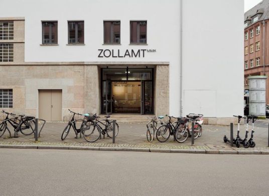 Eingang zum ZOLLAMT MMK mit Fahrradständern und Straße davor